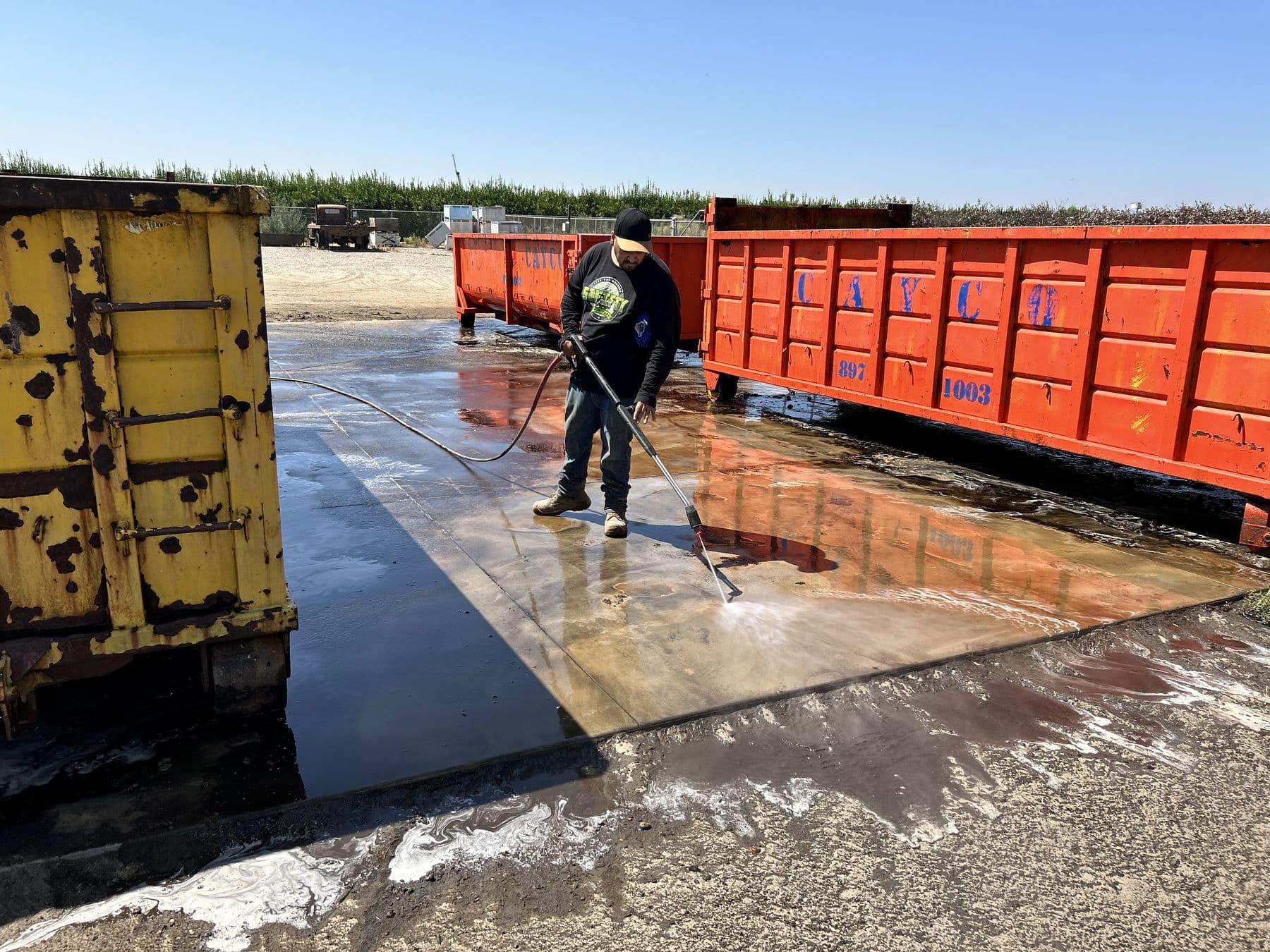 Crew member pressure washing a concrete pad next to roll-off dumpsters