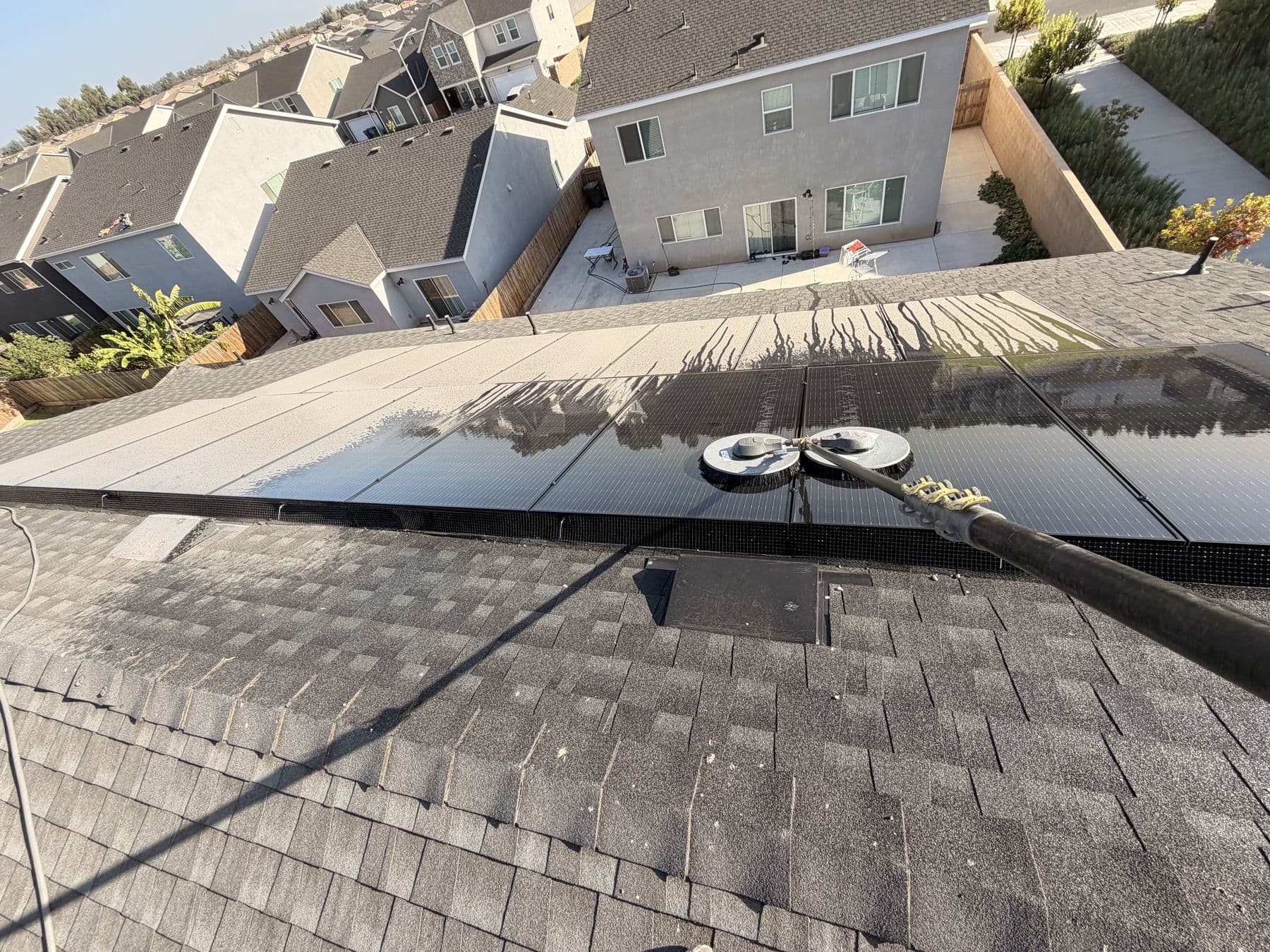Rotary brush cleaning rooftop solar panels on a shingle roof